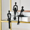 A set of black abstract thinker sculptures displayed on a gold shelf with books.