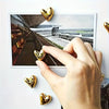 Eine Hand berührt ein gerahmtes Foto eines architektonischen Innenraums mit goldfarbenen herzförmigen Kühlschrankmagneten