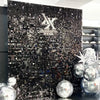 Fond mural en sequins brillants foncés avec un logo 'X' stylisé et des sequins argentés et noirs.