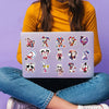 A laptop displaying a set of digital circus themed stickers on a purple background, held by a person wearing a yellow top and