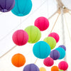 A collection of colorful round paper lanterns in shades of pink, green, blue, and purple hanging from a white structure.