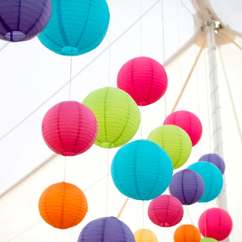 A collection of colorful round paper lanterns in shades of pink, green, blue, and purple hanging from a white structure.