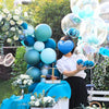 A woman holds a cluster of blue and teal clear bubble balloons in an outdoor garden setting.