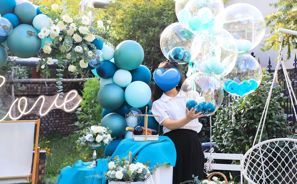 A woman holds a cluster of blue and teal clear bubble balloons in an outdoor garden setting.