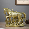 A golden sculpture of a horse with a saddle standing on a wooden fence and landscape.