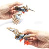 A hand holds an articulated 3D printed owl figurine with detailed feathers and orange beak, used as desk decor.