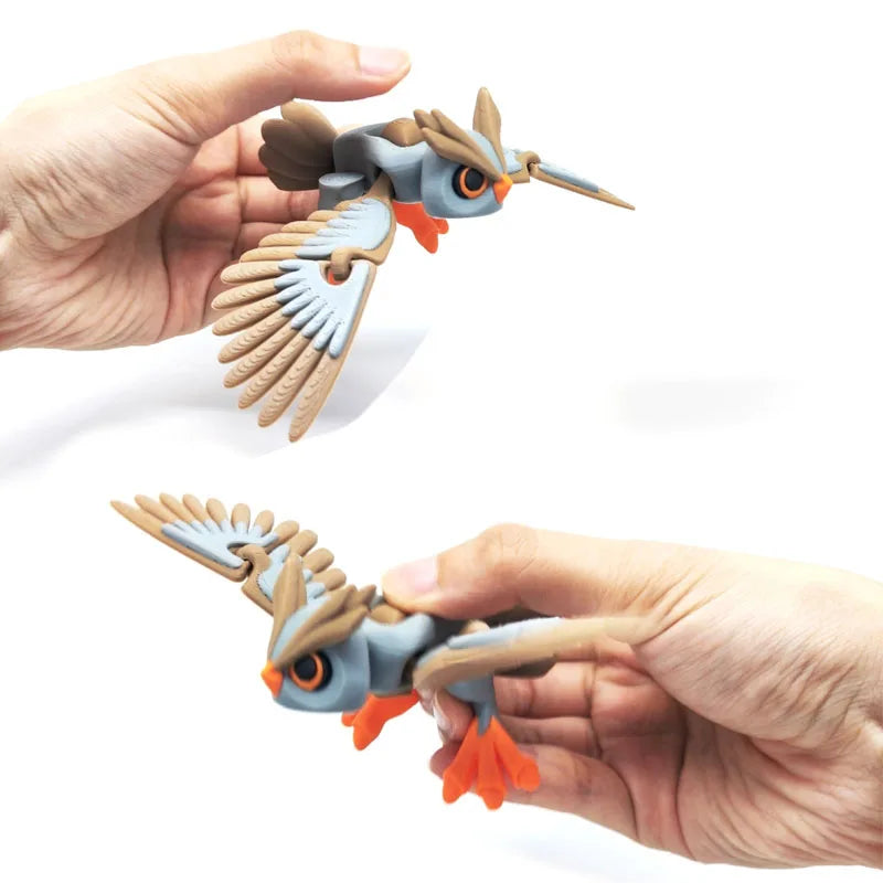 A hand holds an articulated 3D printed owl figurine with detailed feathers and orange beak, used as desk decor.