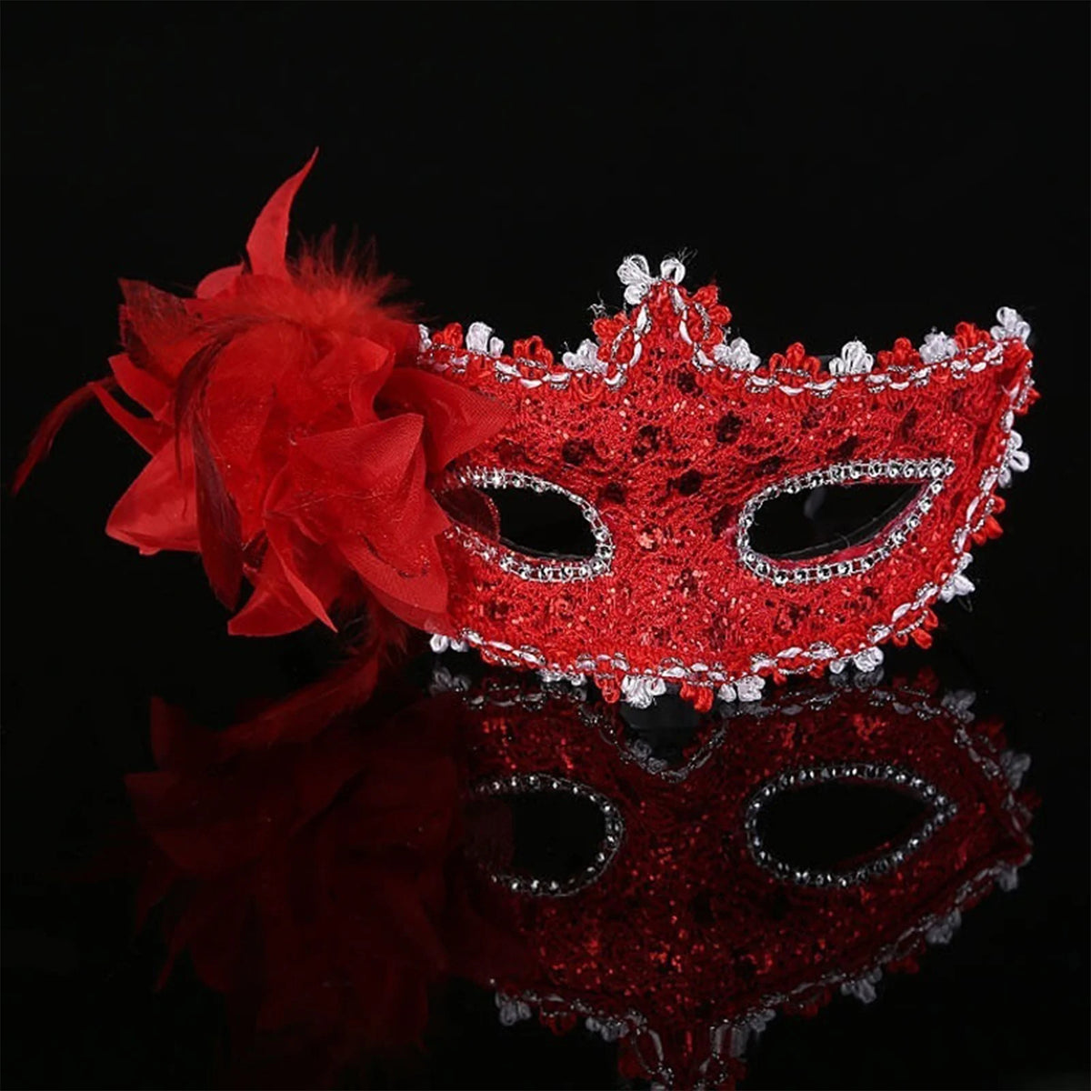 A red feather rhinestone masquerade mask with a large red flower detail, reflected on a dark surface.