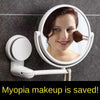 A white, round vanity mirror with a rotating lens is mounted on a gray wall, showing a woman's face.