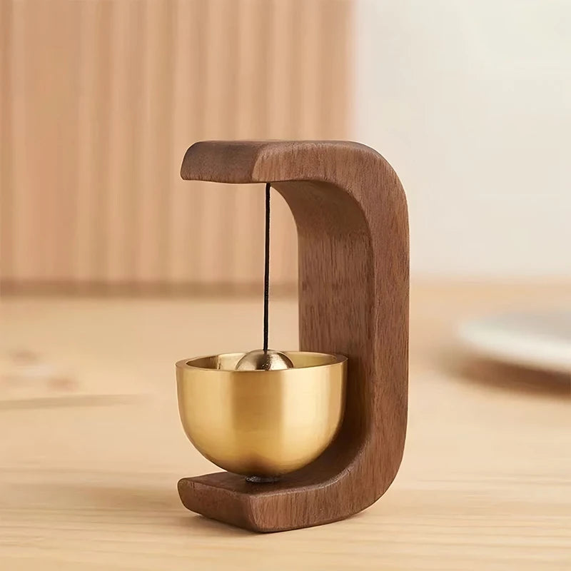 A wooden doorbell featuring a brass bell, designed with a curved wooden frame.