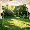 A wedding arch backdrop frame with greenery and string lights suspended under a sheer white fabric canopy in an outdoor garde