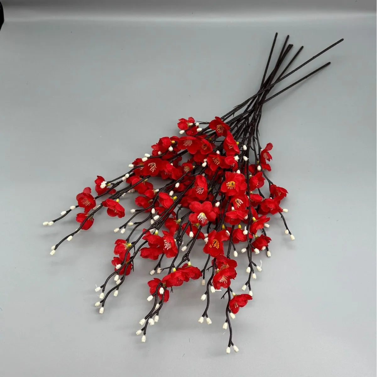 A cluster of artificial red plum blossoms on thin black branches.