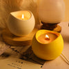 A yellow silicone arc candle jar sits on a white surface next to a lit candle and a weekly diary.