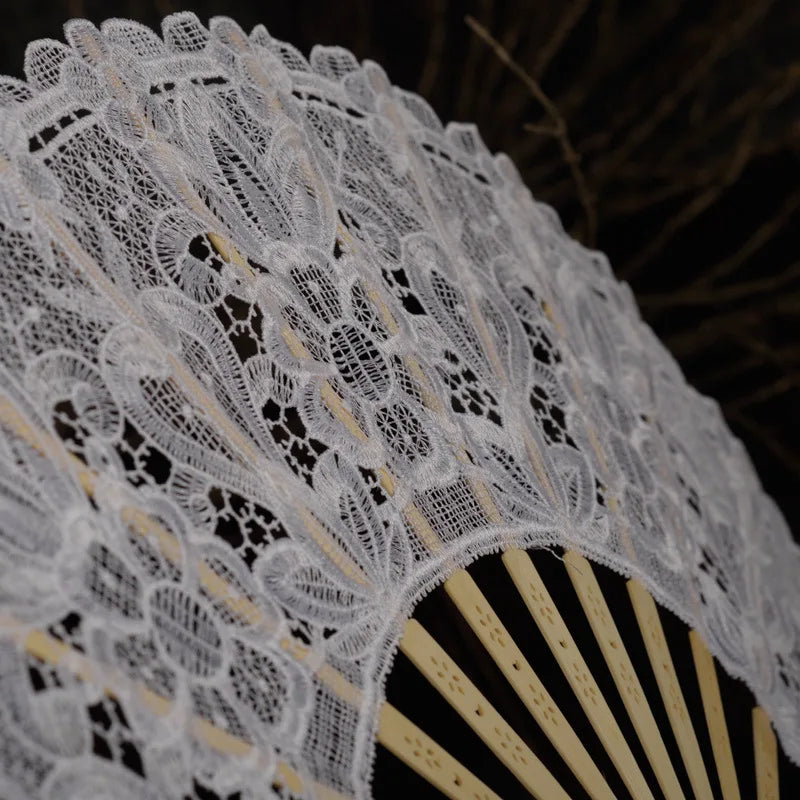 Close-up of an elegant white lace folding hand fan with radiating ribs.