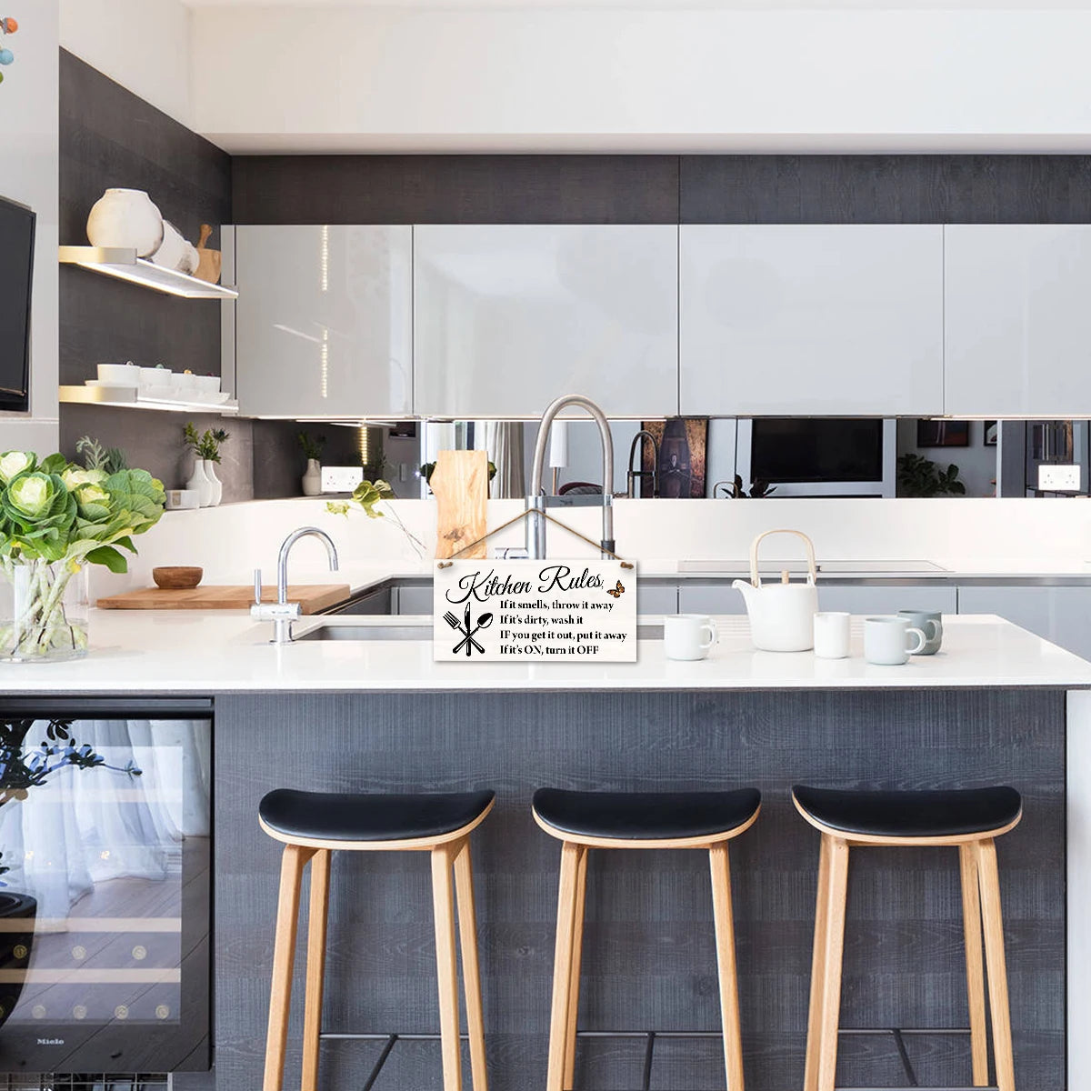 A wooden hanging sign with kitchen rules displayed on a counter in a modern kitchen setting.