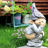 A small statue of a gnome with a pointed hat and beard sitting in green grass near potted plants.