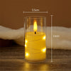 A tall glass candle holder containing a glowing yellow LED star string candle with a visible flame, set on a wooden surface.
