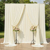 A cream satin backdrop curtain with vertical pleats and floral arrangements used for parties and photography.