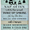 A rustic wooden sign with black text listing camping rules and activities like watching the sunset, sitting by the fire, and 