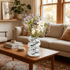 A silver disco ball spiral vase filled with purple and white flowers sits on a wooden coffee table.