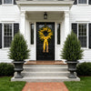 A black front door surrounded by white columns and flanked by tall green topiary trees on a stone walkway.