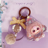 A fluffy pink and gray heart plush keychain charm with a round pink face and a brown leather keyring.