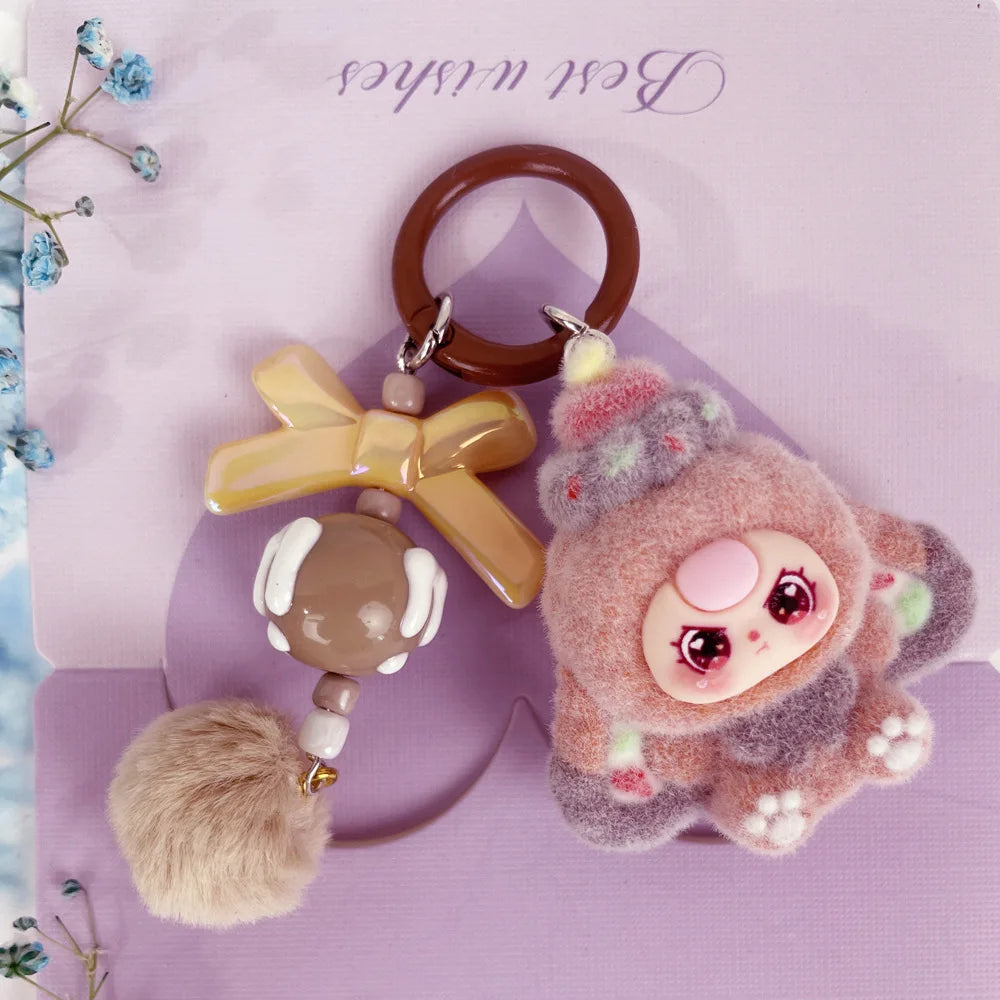 A fluffy pink and gray heart plush keychain charm with a round pink face and a brown leather keyring.