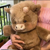 Un jouet en peluche de veau des Highlands brun kawaii est tenu par une personne vêtue d'une robe rose.