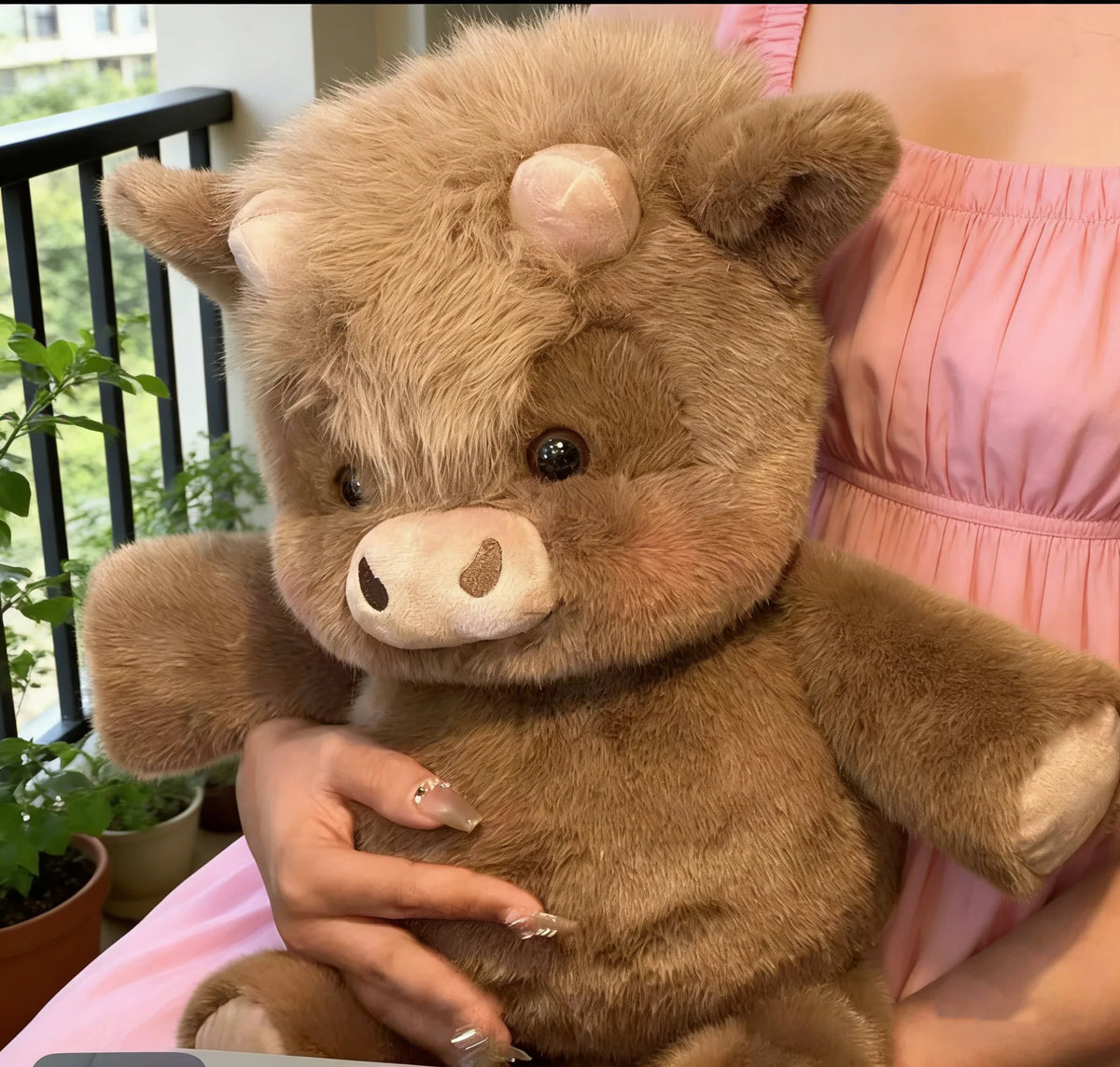 Un jouet en peluche de veau des Highlands brun kawaii est tenu par une personne vêtue d'une robe rose.