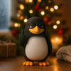 A black and white penguin desk statue with an orange beak and raised flipper sitting on a wooden surface in front of a blurre