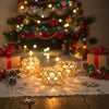 A set of gold crystal votive candle holders resting on a white cloth with pinecones and holiday decorations.