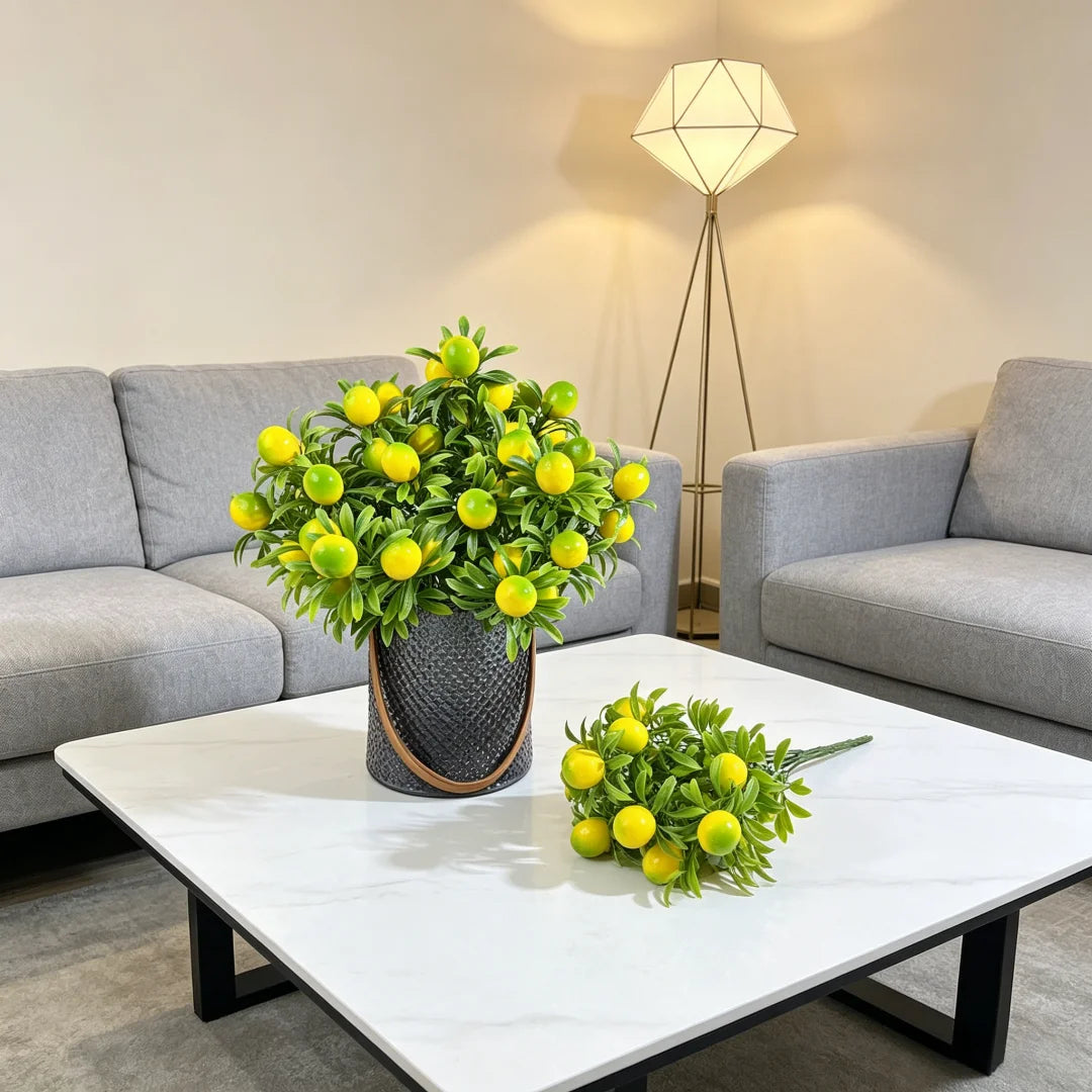 A decorative arrangement of artificial lemon branches in a dark pot displayed on a white table.