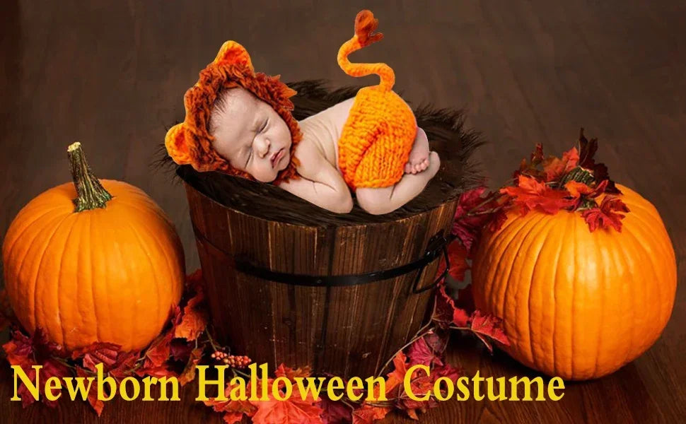 A newborn baby wearing an orange crocheted lion costume resting in a pumpkin basket surrounded by autumn leaves.
