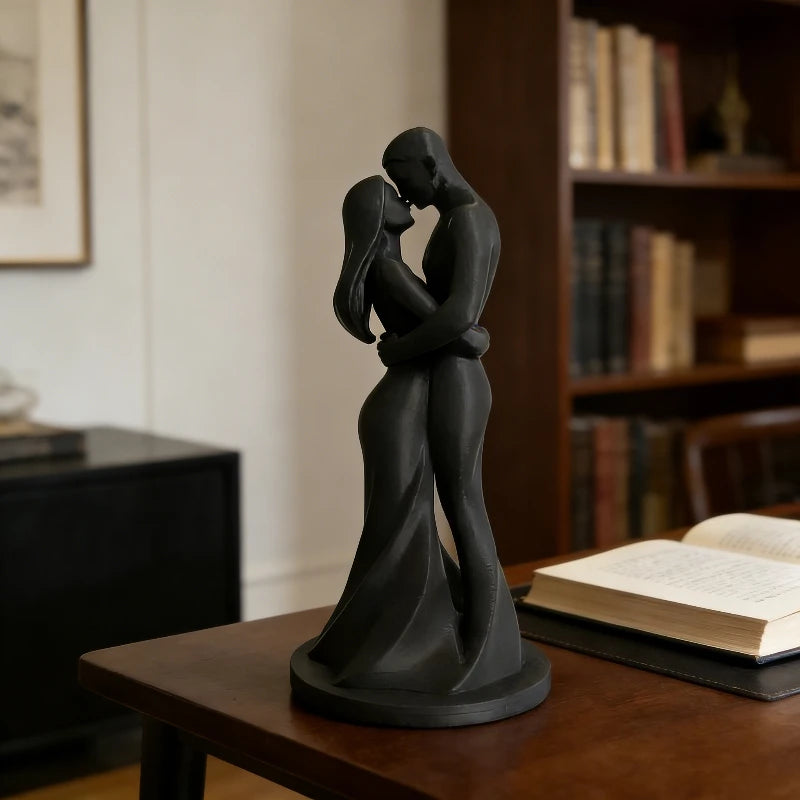 A dark bronze sculpture of a romantic couple embracing and kissing, displayed on a wooden table.