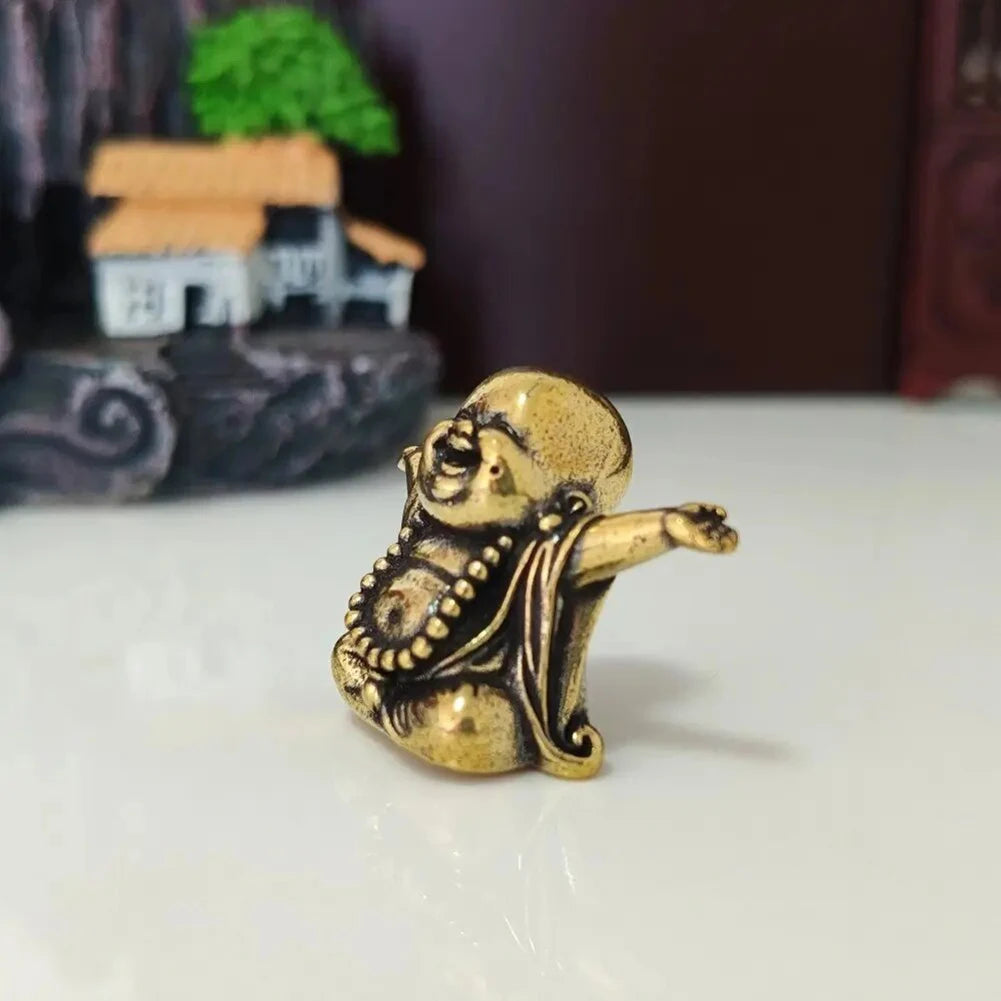 A small brass statue of a laughing Buddha with expressive features, placed on a white surface.