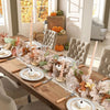 A wooden table displays an artificial maple leaf garland and decorative pumpkins in a bright room.