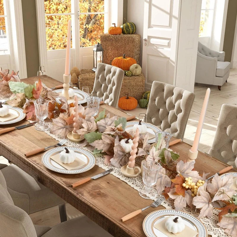 A wooden table displays an artificial maple leaf garland and decorative pumpkins in a bright room.