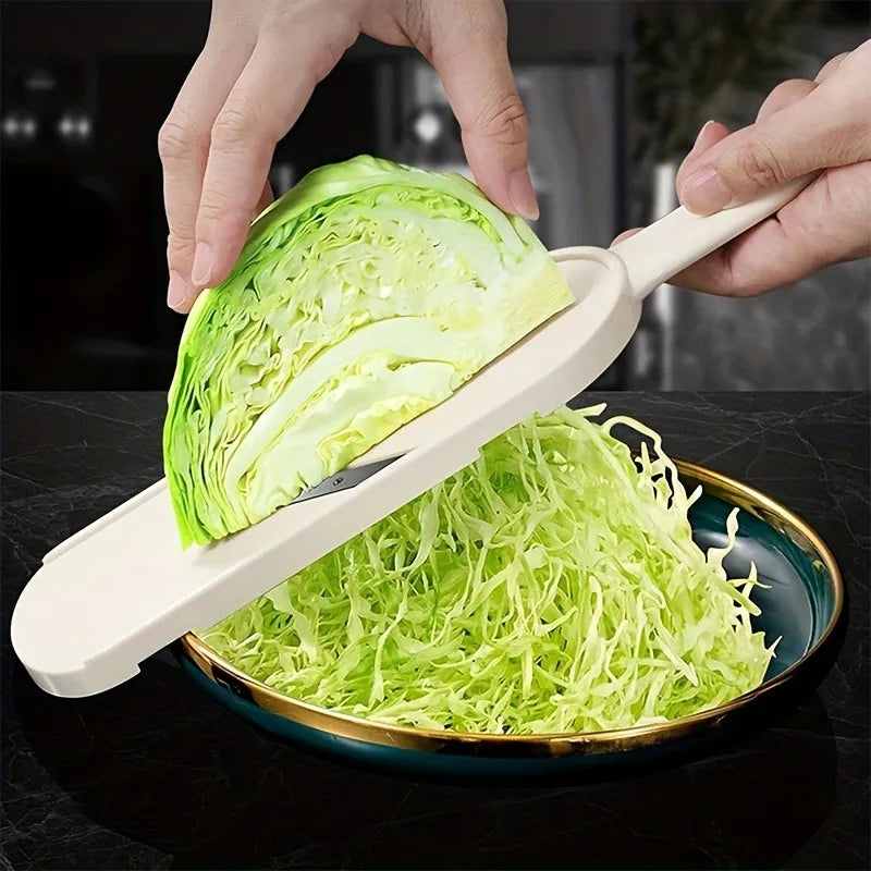 A hand is using a manual cabbage shredder with stainless steel blades to shred a head of green cabbage onto a plate.
