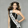 A smiling woman wearing a silver rhinestone birthday crown and glitter sash against a gray background.