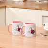 A white ceramic coffee mug with a pink handle and a floral design featuring red roses and gold accents.