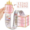 A hand holds a pink birthday cake topper with the number 18 and a ribbon of $100 bills tied around a pink gift box.
