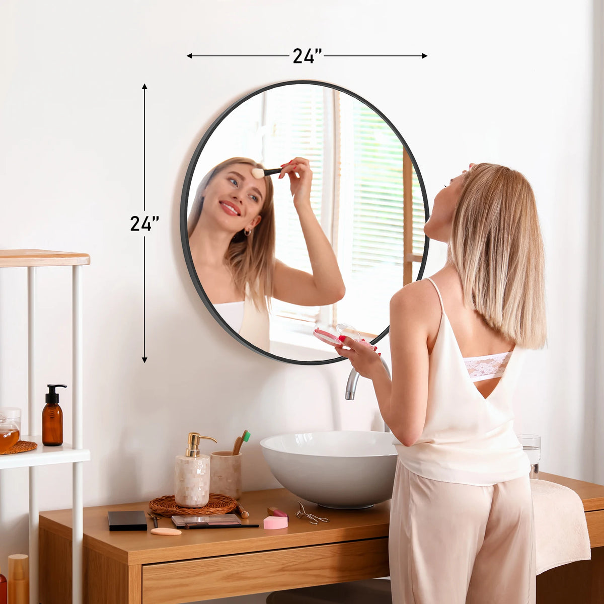 A woman is looking in a large round vanity mirror with a matte metal frame in a bright bathroom setting.