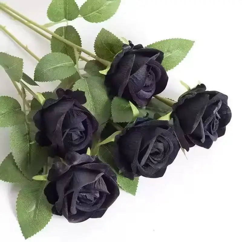 A cluster of dark black velvet artificial roses on green leaves.
