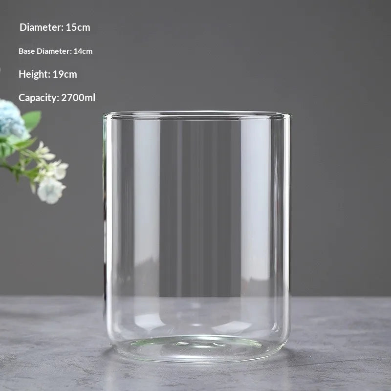 A clear glass cylinder with a wide opening, used as a decor vase for plants.
