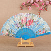 A light blue silk flower folding fan decorated with pink and white floral patterns, displayed on a wooden stand.