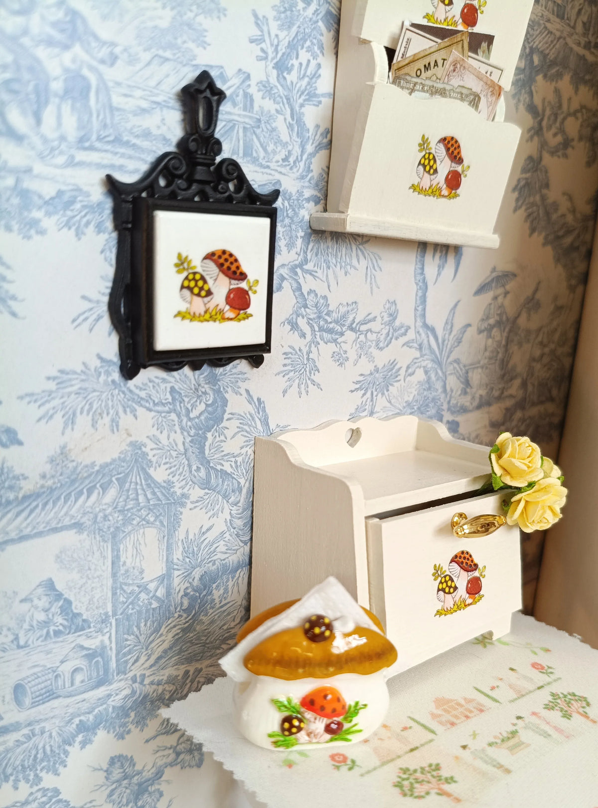 A handcrafted miniature mushroom tableware set displayed on a white cloth next to a decorative wall mount.