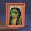 A cute green frog is displayed inside a wooden photo frame.