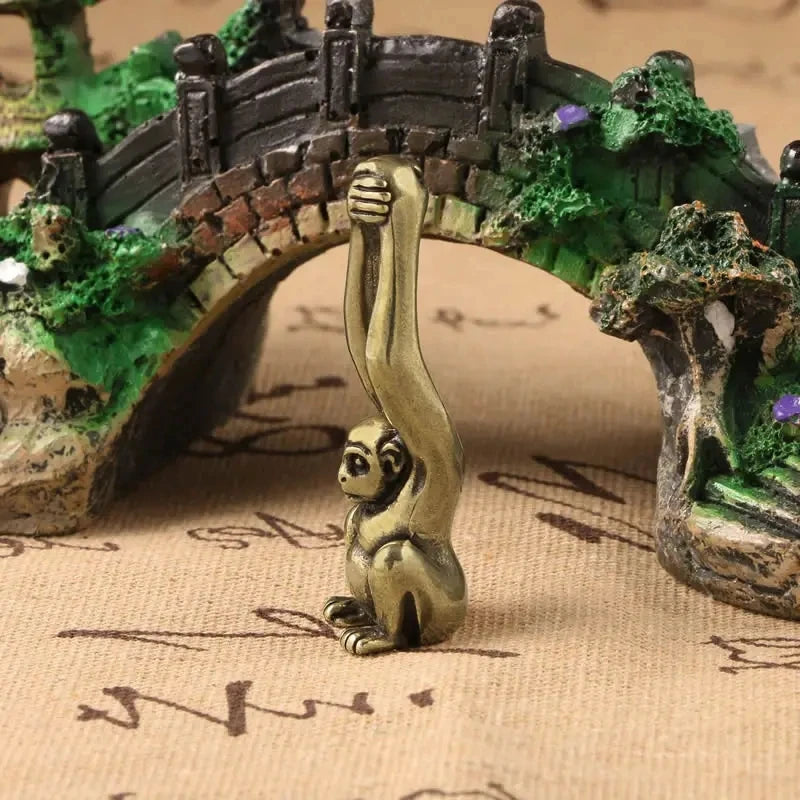 Vintage brass monkey key chain charm hanging from a mossy wooden bridge structure.