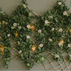 A lush green artificial eucalyptus garland with white flowers draped across a beige wall.