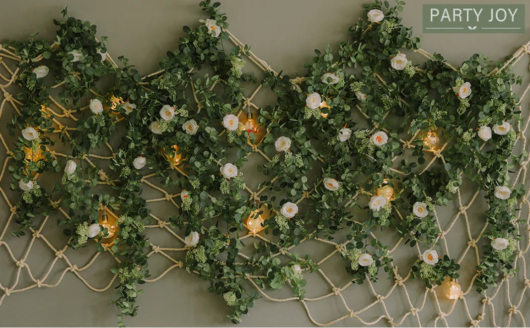 A lush green artificial eucalyptus garland with white flowers draped across a beige wall.